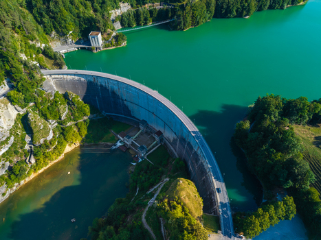 Aerial view of the Barrage de Rossens dam curving across the turquoise waters of Lac de la Gruyere surrounded by lush green forests in Pont la Ville Fribourg Switzerland.