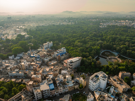 Aerial view of dense residential buildings lush green trees and a small pond in Udaipur Rajasthan India.