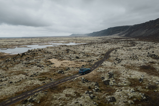 Aerial view of a car driving on a dirt road through the mossy volcanic landscape near Hlidarvatn lake in Sveitarfelagid Olfus Iceland. Aerial view of a car driving on a dirt road through the mossy volcanic landscape near Hlidarvatn lake in Sveitarfelagid Olfus Iceland.