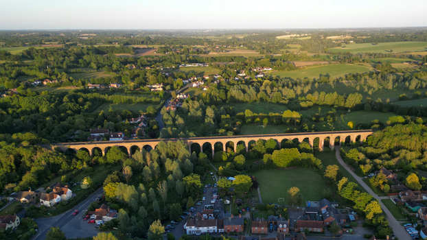 Aerial view of Chappel Viaduct spanning the lush green countryside with its iconic brick arches under the warm light of the golden hour in Chappel England United Kingdom.