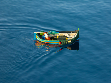 Aerial view of a small brightly colored boat adrift in the vast deep blue sea reflecting sunlight like scattered jewels Ghajnsielem Gozo Malta. Aerial view of a small brightly colored boat adrift in the vast deep blue sea reflecting sunlight like scattered jewels Ghajnsielem Gozo Malta.