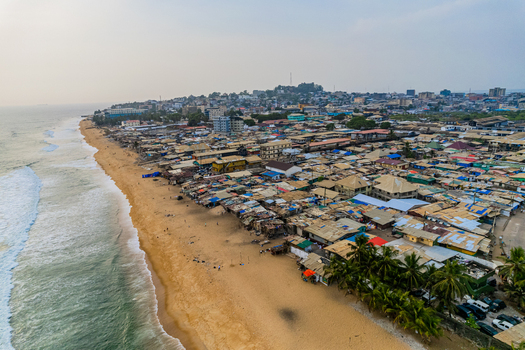 Aerial view of the dense coastal neighborhood and sandy beach with waves crashing on the shore under a hazy sky in Monrovia Montserrado Liberia. Aerial view of the dense coastal neighborhood and sandy beach with waves crashing on the shore under a hazy sky in Monrovia Montserrado Liberia.