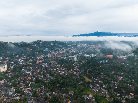 Aerial view of Kandy city with dense residential buildings lush tropical greenery and low hanging mist over the surrounding mountains Kandy Central Province Sri Lanka. Aerial view of Kandy city with dense residential buildings lush tropical greenery and low hanging mist over the surrounding mountains Kandy Central Province Sri Lanka.