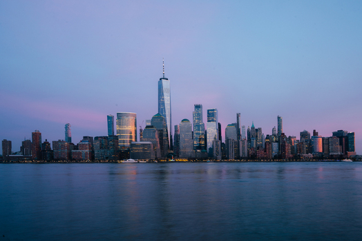 View of the One World Trade Center and the Manhattan skyline at dusk with illuminated skyscrapers reflecting over the Hudson River in New York New York United States.