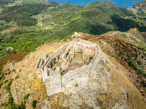 Aerial view of Castello del Volterraio an ancient stone fortress perched on a rocky hilltop surrounded by lush Mediterranean vegetation and rolling hills in Portoferraio Toscana Italy.
