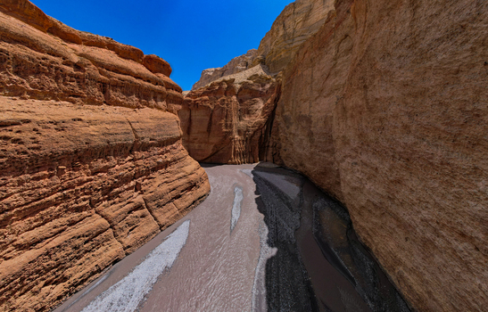 Aerial view of a narrow canyon with steep layered rock walls and a river flowing through the bottom under a clear blue sky in Nepal.
