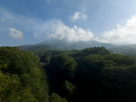 Aerial view of the Tambang Pasir Merapi Kali Gendol Sand Mine surrounded by dense tropical forest with Mount Merapi under a cloudy sky Kecamatan Cangkringan Daerah Istimewa Yogya Indonesia. Aerial view of the Tambang Pasir Merapi Kali Gendol Sand Mine surrounded by dense tropical forest with Mount Merapi under a cloudy sky Kecamatan Cangkringan Daerah Istimewa Yogya Indonesia.
