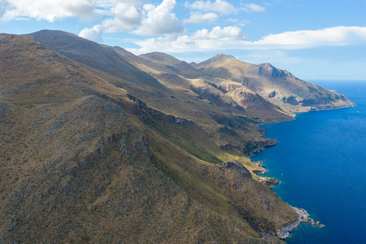 Aerial view of the rugged coastline of Riserva Naturale Orientata dello Zingaro with steep cliffs dry grassy slopes and the deep blue Tyrrhenian Sea in San Vito Lo Capo Sicilia Italy. Aerial view of the rugged coastline of Riserva Naturale Orientata dello Zingaro with steep cliffs dry grassy slopes and the deep blue Tyrrhenian Sea in San Vito Lo Capo Sicilia Italy.