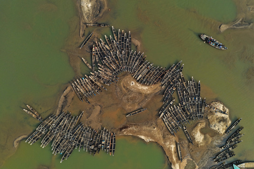 Aerial view of numerous wooden boats moored along the sandy banks of the Jadukata River in Sunamganj Sylhet Division Bangladesh. Aerial view of numerous wooden boats moored along the sandy banks of the Jadukata River in Sunamganj Sylhet Division Bangladesh.