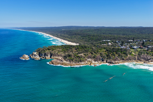 Aerial view of North Stradbroke Island featuring a rocky headland turquoise ocean waves crashing against the sandy coastline and lush coastal vegetation in Redland City Queensland Australia. Aerial view of North Stradbroke Island featuring a rocky headland turquoise ocean waves crashing against the sandy coastline and lush coastal vegetation in Redland City Queensland Australia.