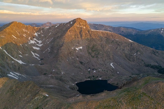 Aerial view of Mount of the Holy Cross in the Sawatch Range featuring rugged peaks rocky slopes with snow and a dark alpine lake under golden hour light in Vail Colorado United States. Aerial view of Mount of the Holy Cross in the Sawatch Range featuring rugged peaks rocky slopes with snow and a dark alpine lake under golden hour light in Vail Colorado United States.