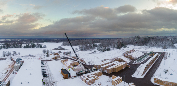 Aerial view of a lumber yard with stacks of timber and a mobile crane lifting a modular structure on a snow covered industrial site in Latvia. Aerial view of a lumber yard with stacks of timber and a mobile crane lifting a modular structure on a snow covered industrial site in Latvia.
