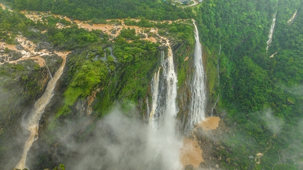 Aerial view of Jog Falls cascading down rocky cliffs surrounded by lush green forests and mist in Kargal Karnataka India.