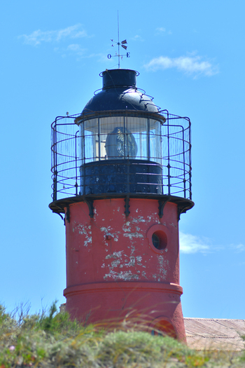 View of the red Puerto Piramides lighthouse with its black lantern room and weather vane under a clear blue sky Puerto Madryn Chubut Argentina. View of the red Puerto Piramides lighthouse with its black lantern room and weather vane under a clear blue sky Puerto Madryn Chubut Argentina.