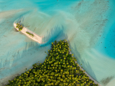 Aerial view of a lush tropical island with dense palm trees and a small sandy islet surrounded by turquoise lagoon water in Moorea Maiao Windward Islands French Polynesia. Aerial view of a lush tropical island with dense palm trees and a small sandy islet surrounded by turquoise lagoon water in Moorea Maiao Windward Islands French Polynesia.