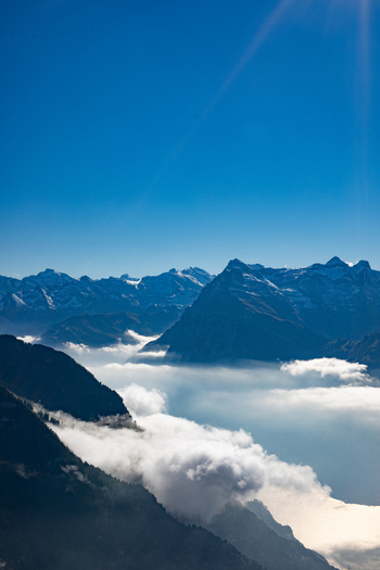 Aerial view of the Swiss Alps with rugged mountain peaks rising above a thick sea of clouds under a clear blue sky in Airolo Ticino Switzerland. Aerial view of the Swiss Alps with rugged mountain peaks rising above a thick sea of clouds under a clear blue sky in Airolo Ticino Switzerland.