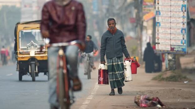 View of a man carrying containers on a street in Bogura Bangladesh. View of a man carrying containers on a street in Bogura Bangladesh.