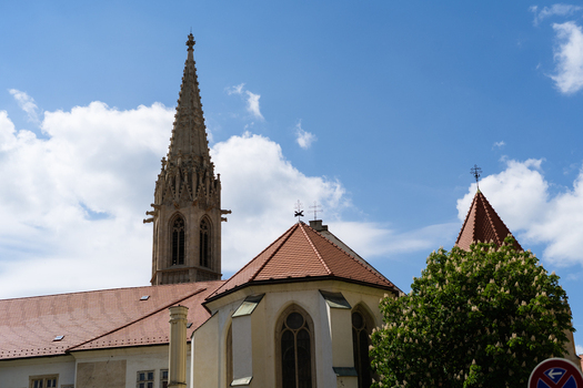 View of the historic Franciscan Church with its ornate Gothic spire and red tiled roofs under a blue sky with white clouds in Bratislava Bratislava Region Slovakia. View of the historic Franciscan Church with its ornate Gothic spire and red tiled roofs under a blue sky with white clouds in Bratislava Bratislava Region Slovakia.