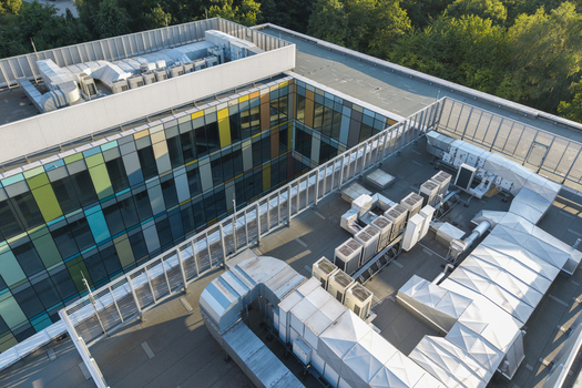 Aerial view of the AI data center cooling system featuring rows of HVAC units and metal ductwork on a modern rooftop with a colorful glass facade in Krakow Lesser Poland Voivode Poland. Aerial view of the AI data center cooling system featuring rows of HVAC units and metal ductwork on a modern rooftop with a colorful glass facade in Krakow Lesser Poland Voivode Poland.