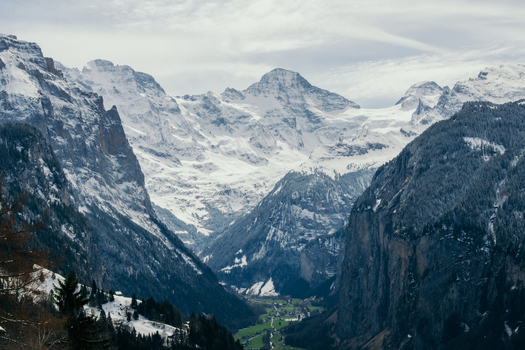 View of snow dusted peaks towering over a lush valley where tiny buildings nestle amidst vibrant green fields in the Swiss Alps Wengen Switzerland. View of snow dusted peaks towering over a lush valley where tiny buildings nestle amidst vibrant green fields in the Swiss Alps Wengen Switzerland.