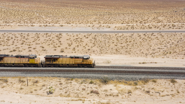 Aerial view of a yellow freight train traveling through the arid desert landscape of the United States.