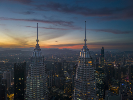 Kuala Lumpur Malaysia 11 March 2026 Aerial view of the Petronas Twin Towers at sunset with the city skyline and distant mountains under a colorful sky.