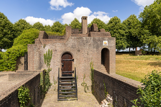 View of a historic brick structure with a wooden door and stairs surrounded by lush greenery and fortification walls in Heusden North Brabant Netherlands.