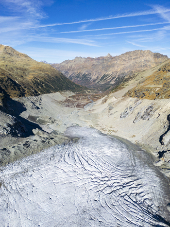 Aerial view of the stark textured Morteratsch Glacier snaking between rugged autumnal mountains under a brilliant blue sky Morteratsch Grisons Switzerland. Aerial view of the stark textured Morteratsch Glacier snaking between rugged autumnal mountains under a brilliant blue sky Morteratsch Grisons Switzerland.