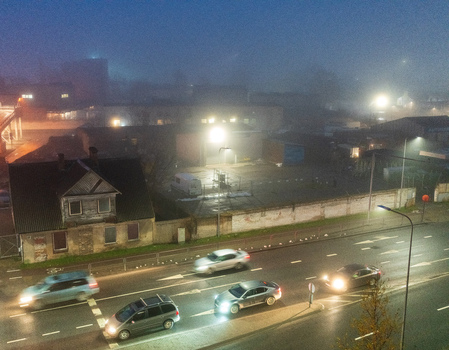 View of a foggy street scene at night with moving cars illuminated by street lights and a historic house in Vilnius Vilnius County Lithuania. View of a foggy street scene at night with moving cars illuminated by street lights and a historic house in Vilnius Vilnius County Lithuania.