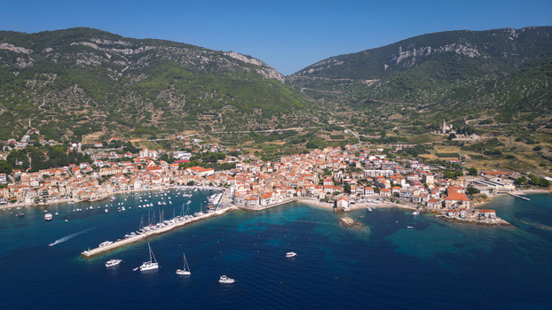 Aerial view of the historic coastal town of Komiza with red roofed houses a busy harbor with boats and lush green mountains under a clear sky in Komiza Split Dalmatia County Croatia.
