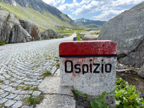 Gotthard Pass Switzerland 16 May 2026 View of a stone marker with the word Ospizio on a cobblestone road leading through the rugged alpine landscape of the Gotthard Pass.
