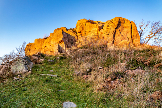 View of the Kincasslagh Mass Rock illuminated by golden hour light surrounded by grassy terrain and dry vegetation in Kincasslagh County Donegal Ireland. View of the Kincasslagh Mass Rock illuminated by golden hour light surrounded by grassy terrain and dry vegetation in Kincasslagh County Donegal Ireland.