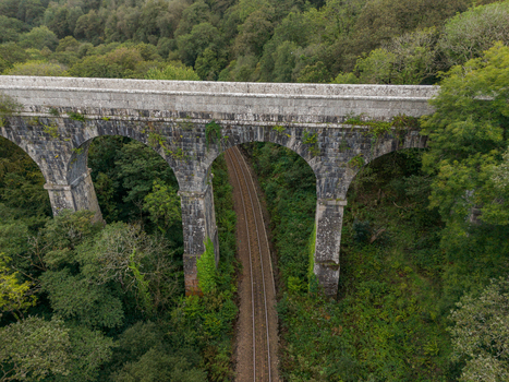 Aerial view of the historic stone arches of the Treffry Viaduct spanning the lush green Luxulyan Valley with railway tracks running beneath in Luxulyan Cornwall United Kingdom.