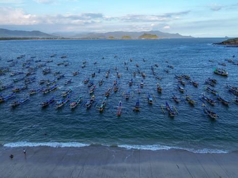 Aerial view of Papuma Beach with numerous traditional fishing boats anchored in the blue bay sandy shoreline and distant hills in Jember East Java Indonesia. Aerial view of Papuma Beach with numerous traditional fishing boats anchored in the blue bay sandy shoreline and distant hills in Jember East Java Indonesia.