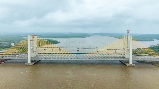 Aerial view of the modern cable stayed Zuari Bridge spanning the Zuari River with lush green banks and cloudy sky in Cortalim Goa India.