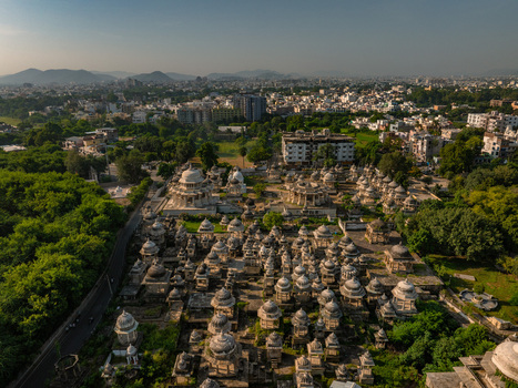 Aerial view of the historic Ahar Cenotaphs featuring numerous stone chhatris surrounded by lush greenery and the urban landscape of Udaipur Rajasthan India.
