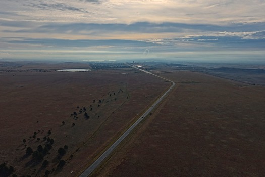 Aerial view of a long highway stretching through a vast dry landscape with scattered trees and a distant horizon under a cloudy sky in Golden Colorado United States.