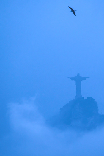 View of the Christ the Redeemer statue silhouette emerging from blue mist with a bird flying above in Rio de Janeiro Rio de Janeiro Brazil.