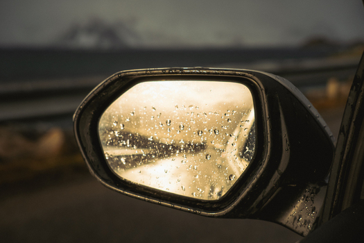 View of raindrops cling to a side mirror reflecting the distant moody coastline under a muted sky creating a blurred scene Henningsv&aelig;r Nordland Norway.