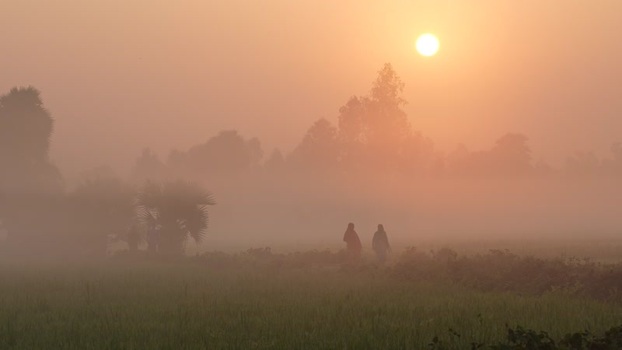 View of people walking through misty fields at sunrise Bangladesh.