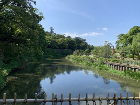 Japan 06 July 2026 View of a calm canal lined with lush green trees and a wooden fence in a park setting. Japan 06 July 2026 View of a calm canal lined with lush green trees and a wooden fence in a park setting.