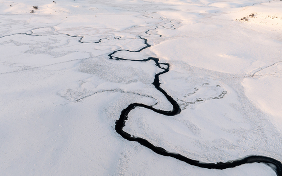 Aerial view of a dark river snaking through a snow covered landscape its icy waters reflecting the pale winter light Nasbinals Occitanie France.