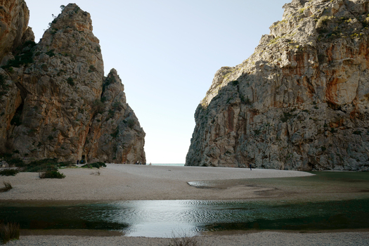 View of the dramatic limestone cliffs of Torrent de Pareis framing the sandy beach and shallow water in Mallorca Balearic Islands Spain.