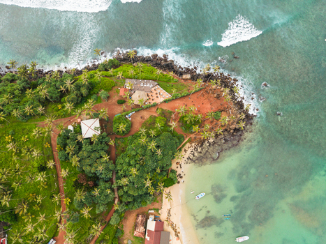 Aerial view of Coconut Tree Hill with lush palm trees reddish soil and turquoise ocean waves crashing against the rocky coastline in Mirissa Southern Province Sri Lanka. Aerial view of Coconut Tree Hill with lush palm trees reddish soil and turquoise ocean waves crashing against the rocky coastline in Mirissa Southern Province Sri Lanka.