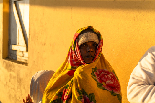 Ratnapura Sri Lanka 23 February 2026 View of a pilgrim wrapped in a yellow floral blanket and beanie standing against a yellow wall at Adam s Peak during sunrise.