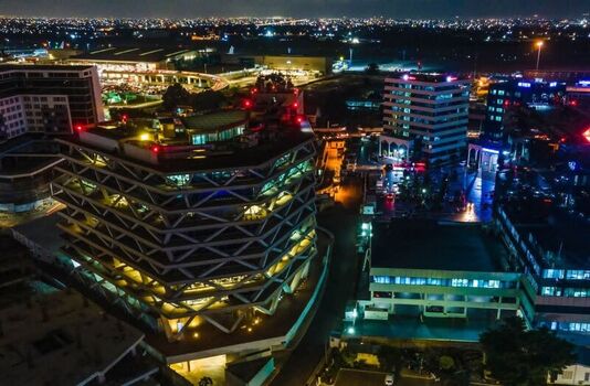 Aerial view of the illuminated One Airport Square building at night showcasing modern architecture and surrounding city lights in Ghana. Aerial view of the illuminated One Airport Square building at night showcasing modern architecture and surrounding city lights in Ghana.