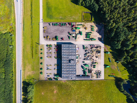 Aerial view of a farm equipment supplier featuring a large industrial warehouse surrounded by agricultural machinery parking areas and green fields in Kekava Kekava Municipality Latvia. Aerial view of a farm equipment supplier featuring a large industrial warehouse surrounded by agricultural machinery parking areas and green fields in Kekava Kekava Municipality Latvia.