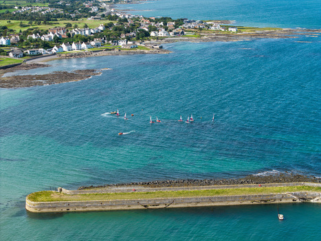 Aerial view of Donaghadee Harbour with small sailboats sailing in the clear blue water along the coastline of Donaghadee Northern Ireland United Kingdom. Aerial view of Donaghadee Harbour with small sailboats sailing in the clear blue water along the coastline of Donaghadee Northern Ireland United Kingdom.