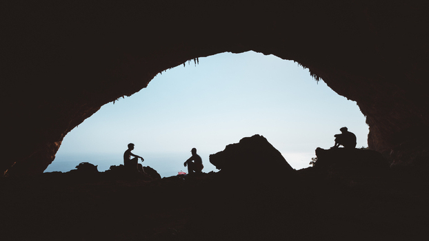 View of silhouettes of three people sitting inside the entrance of Hoq Cave looking out towards the sea in Socotra Socotra Yemen. View of silhouettes of three people sitting inside the entrance of Hoq Cave looking out towards the sea in Socotra Socotra Yemen.