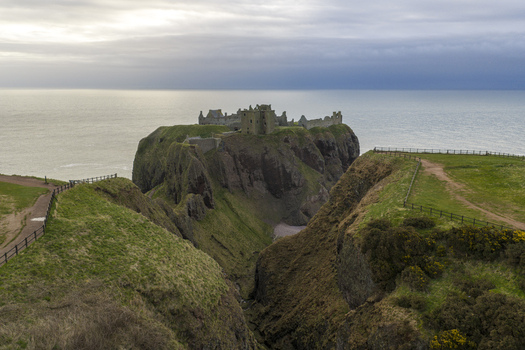 Aerial view of Dunnottar Castle ruins perched on a steep rocky cliff overlooking the North Sea under an overcast sky Stonehaven Scotland United Kingdom. Aerial view of Dunnottar Castle ruins perched on a steep rocky cliff overlooking the North Sea under an overcast sky Stonehaven Scotland United Kingdom.